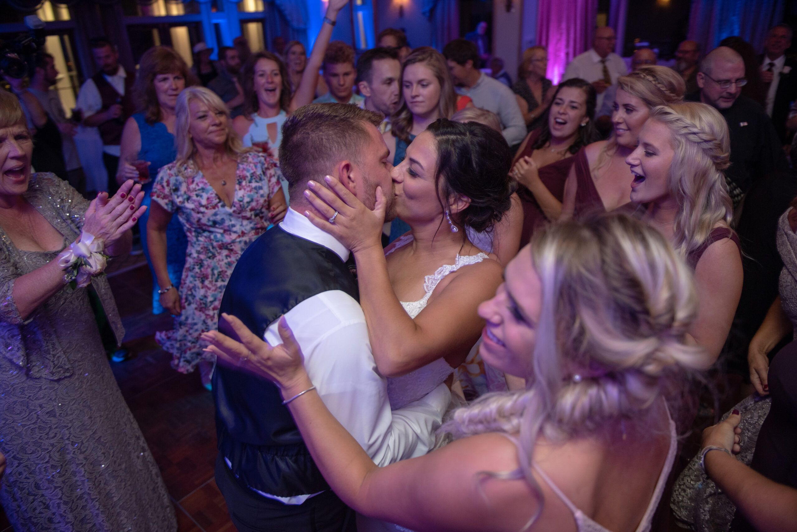 Bride and groom kissing surrounded by cheering guests on the dance floor with purple uplighting at Water's Edge Resort in Westbrook CT