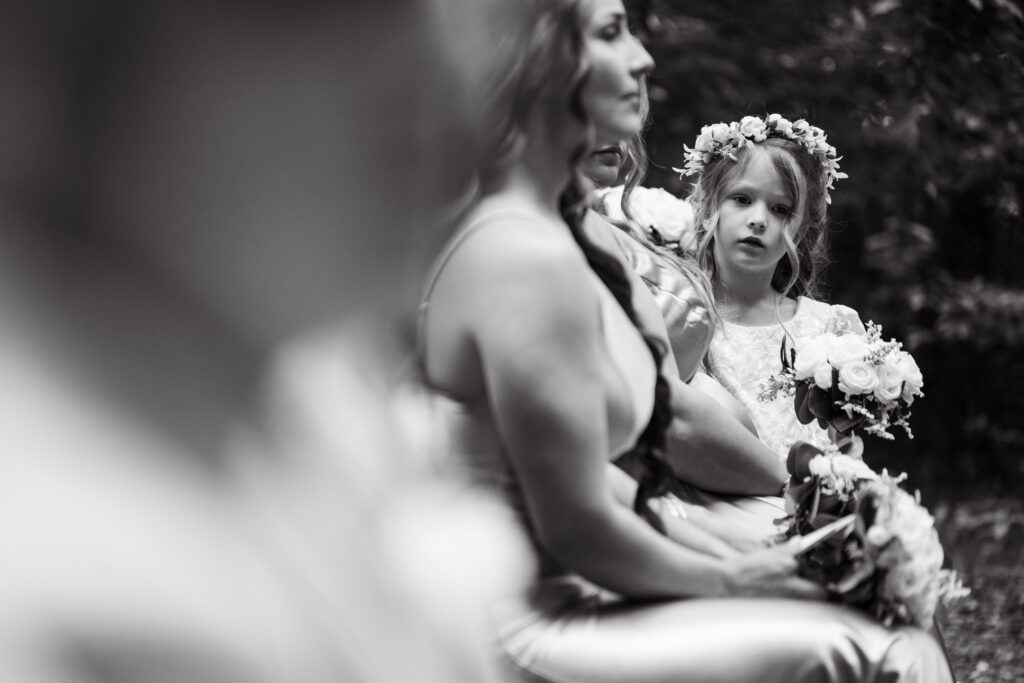 Black and white candid of a flower girl in a flower crown watching the ceremony beside a bridesmaid at Stonehurst at Hampton Valley in Hampton CT