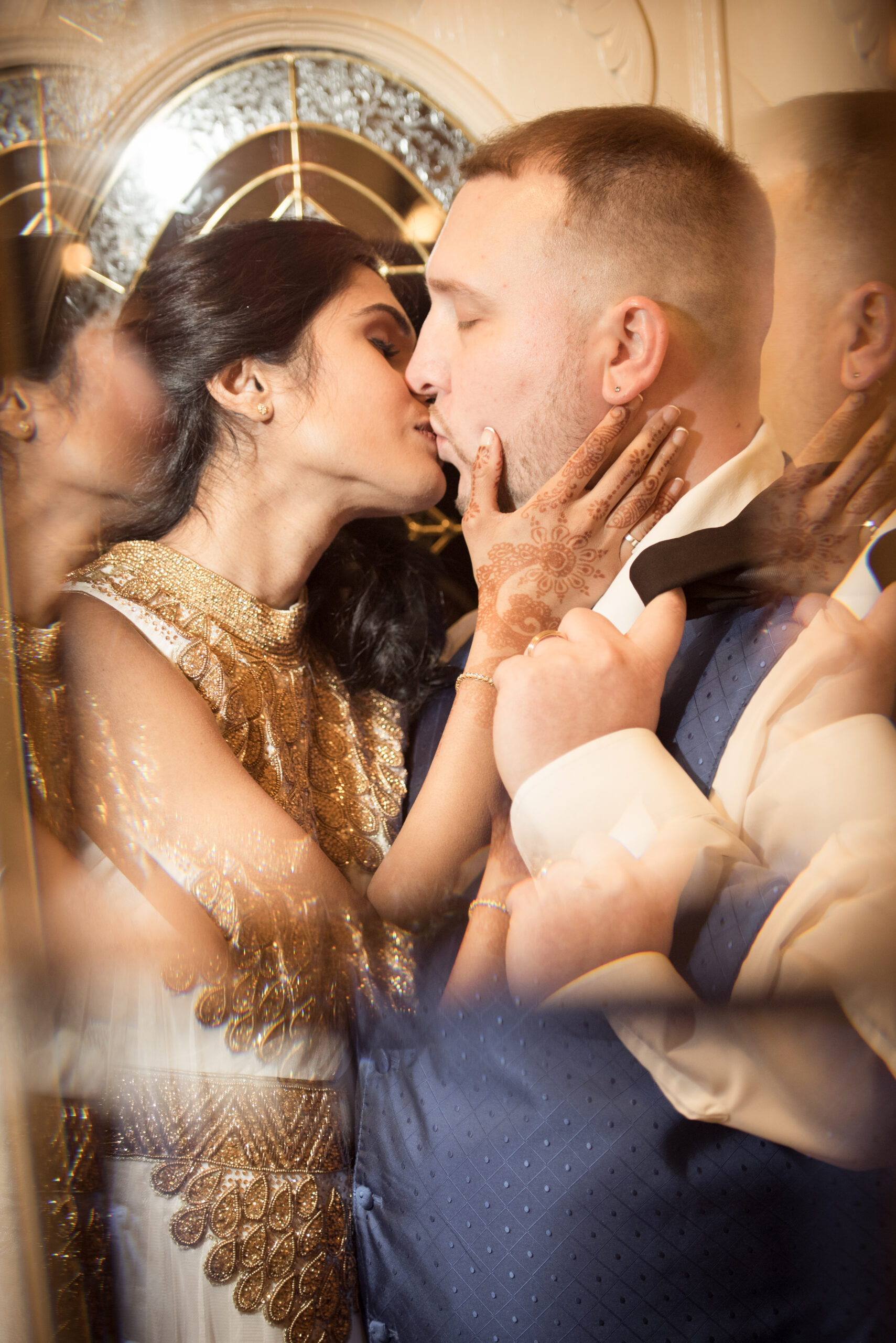 Bride in a gold beaded dress with henna on her hands kissing her groom during a multicultural wedding celebration in Connecticut