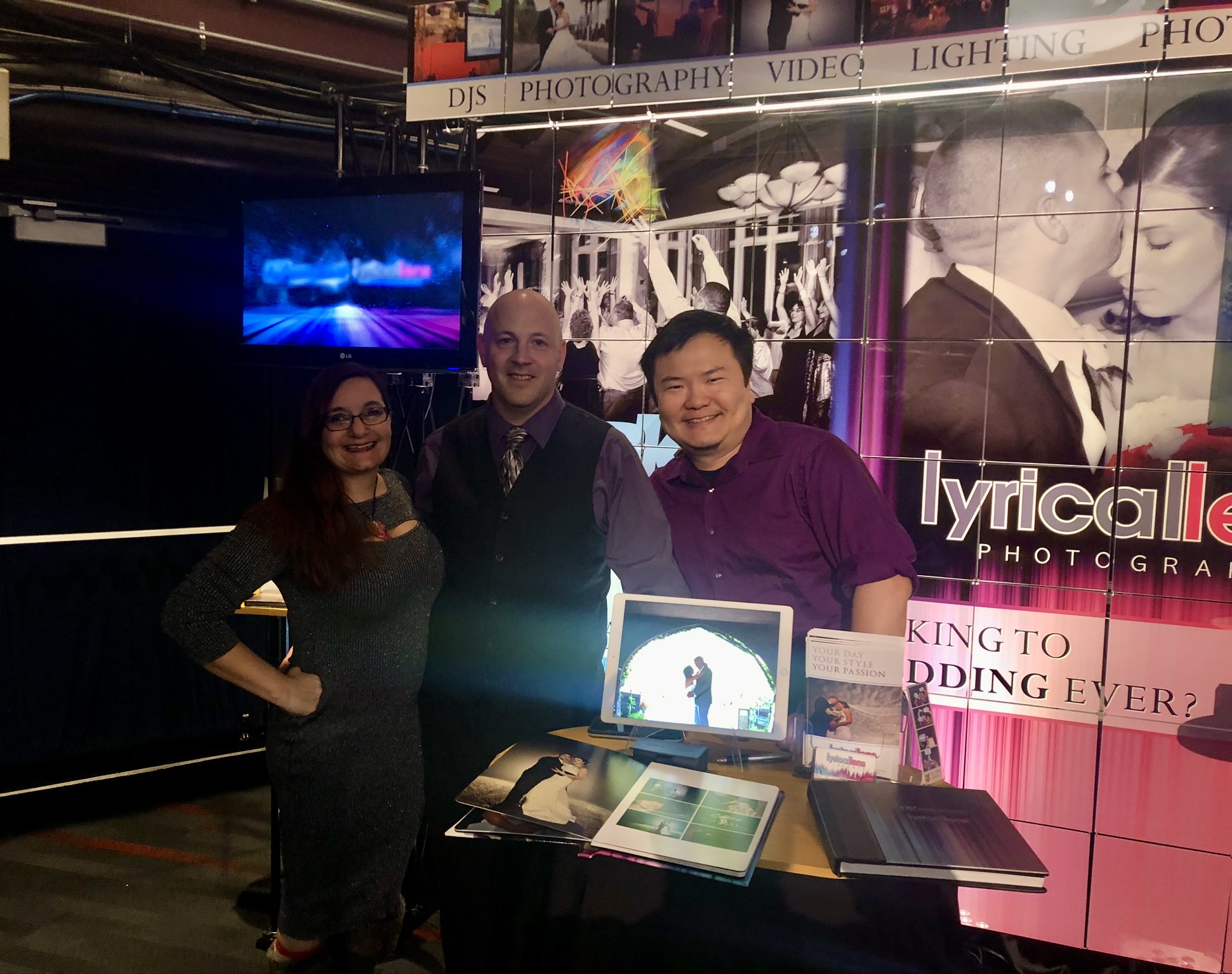 Connie, Dave, and Matt from Lyrical Lens Events at their booth with wedding albums and portfolio display at a Jenks Productions bridal show in Connecticut
