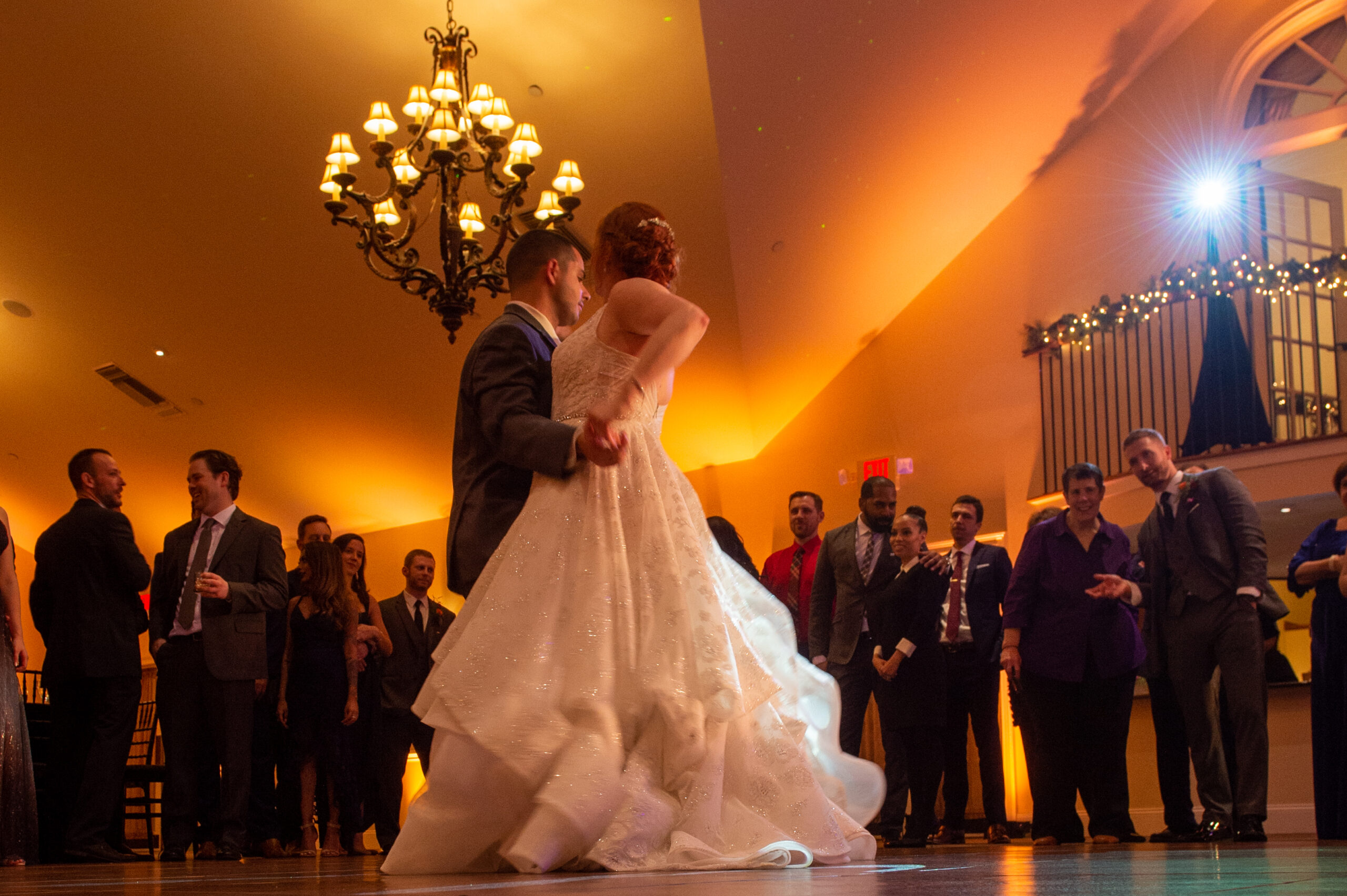 Bride and groom sharing their first dance under a chandelier with warm amber uplighting at Riverhouse at Goodspeed Station in East Haddam CT